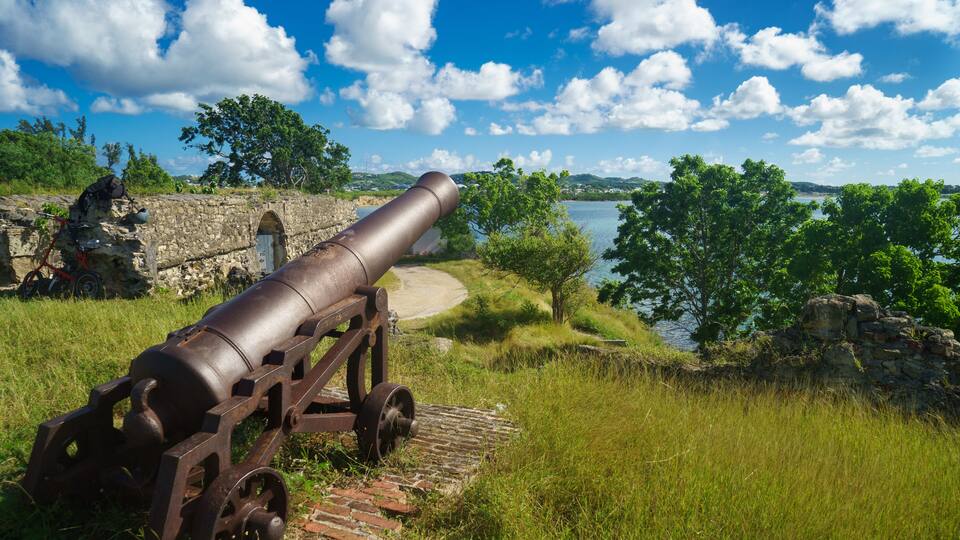 Old cannon in the fort is looking at sea with amazing clouds and island on background