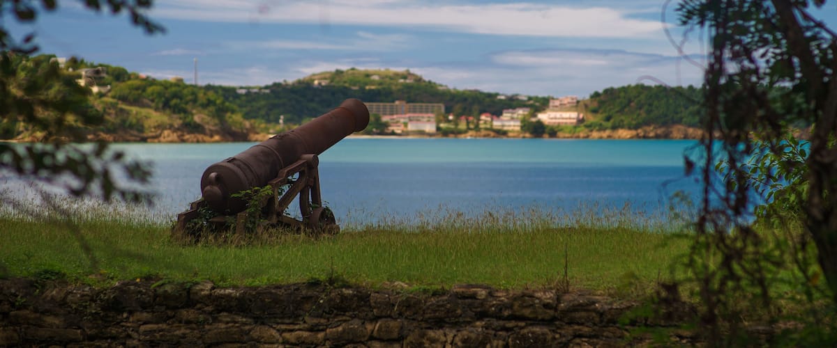 A cannon on a grassy hill overlooking a calm sea with a distant shoreline.