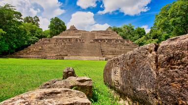 A large stone pyramid structure surrounded by lush green grass and trees.