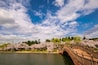 A wooden bridge over a river, cherry blossom trees, and a clear blue sky with clouds.