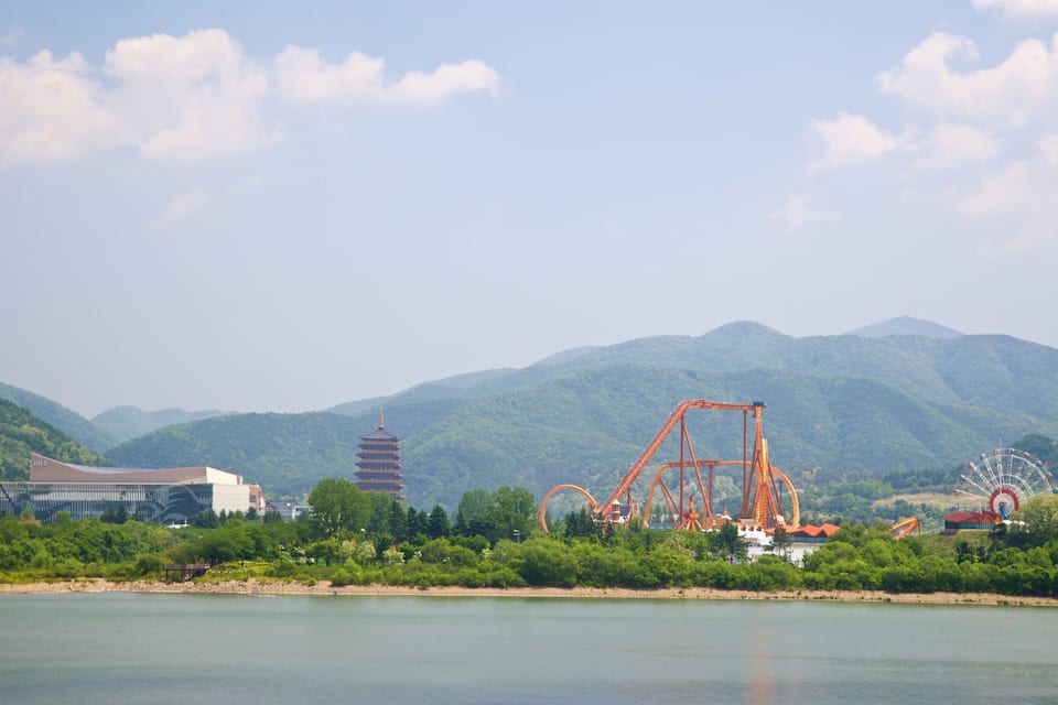 Um parque de diversões à beira-mar, com montanhas-russas, uma roda gigante e um pagode.