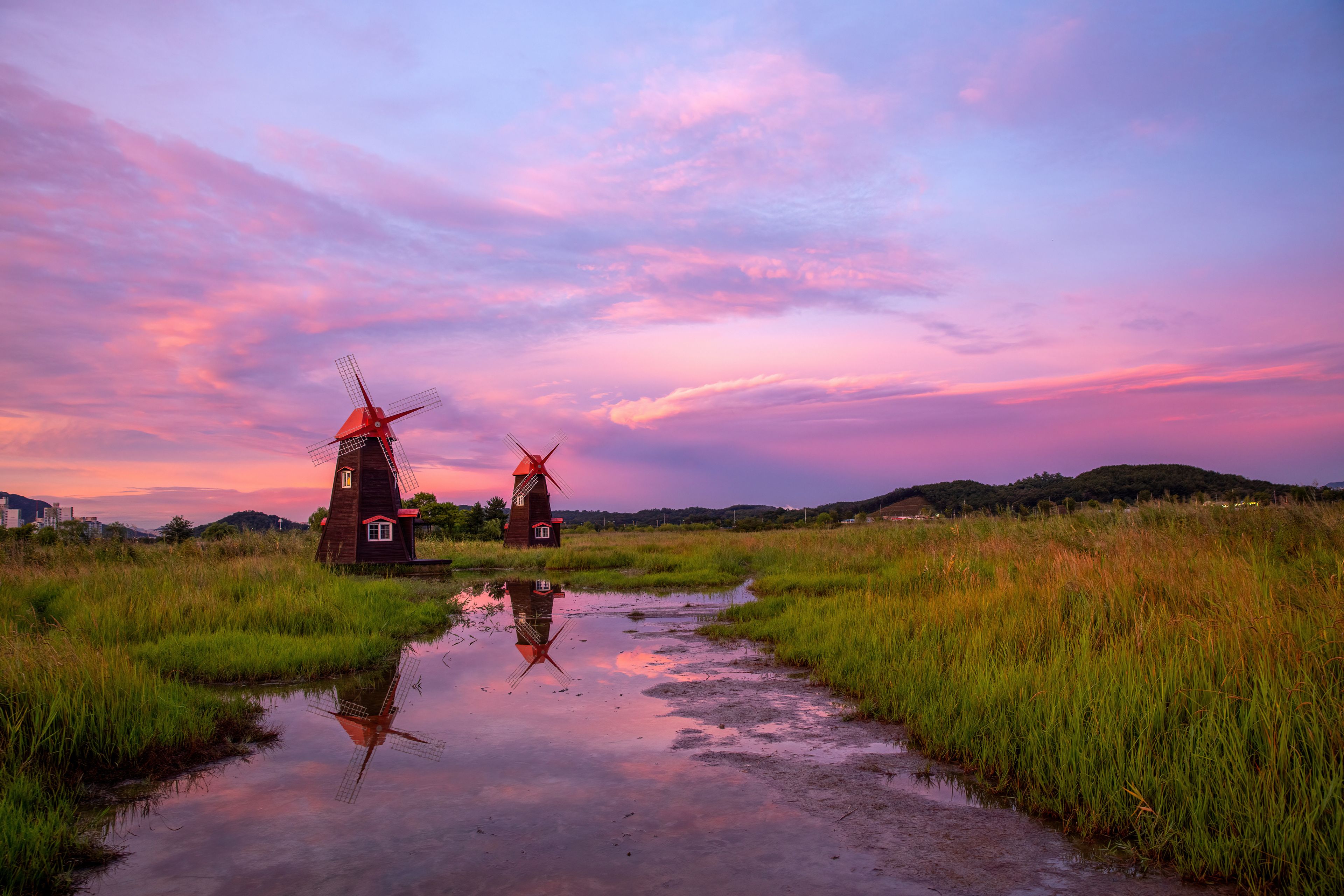 Two windmills in a field with a reflective water surface and a sunset sky.