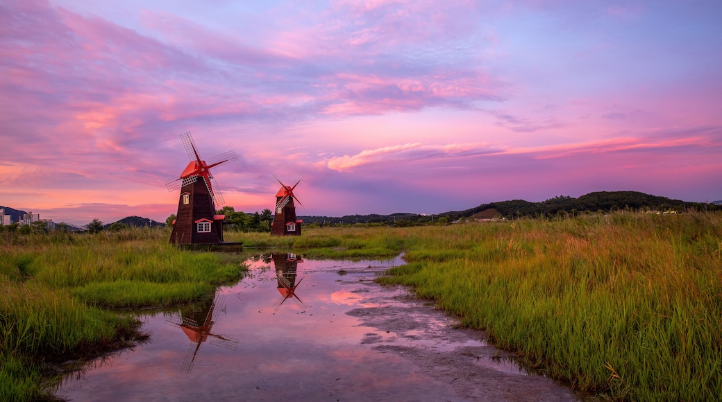 Two windmills in a field with a reflective water surface and a sunset sky.