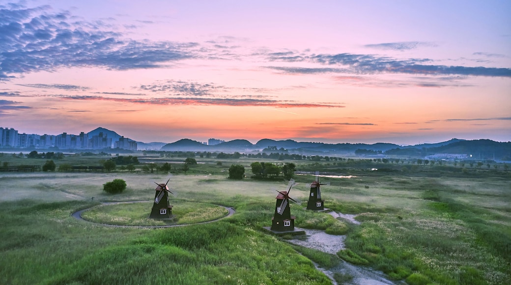 A rural landscape with windmills, green fields, and distant city buildings.