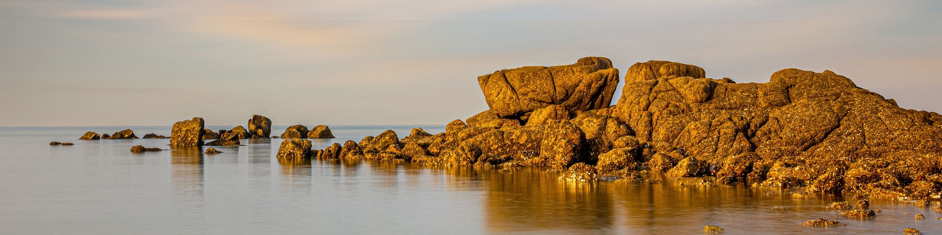 A calm sea with large, rugged rocks and a clear sky.