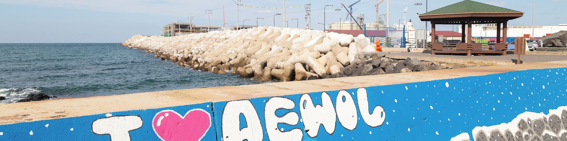 A coastal walkway with a painted message, a gazebo, and a rocky breakwater.