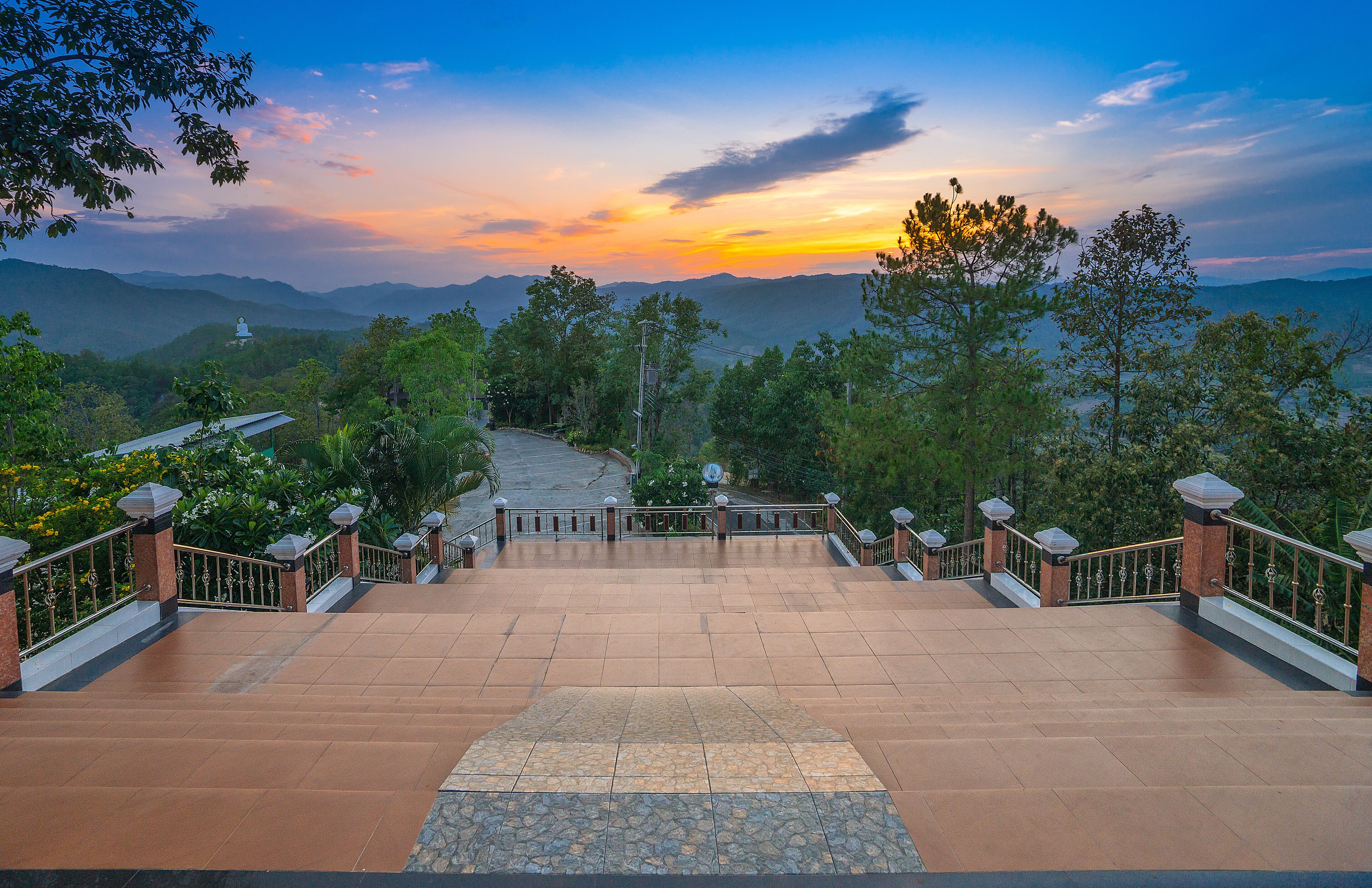 A stone staircase leading to a temple surrounded by lush greenery and mountains.
