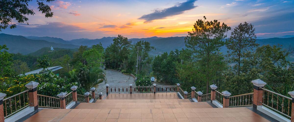 A stone staircase leading to a temple surrounded by lush greenery and mountains.