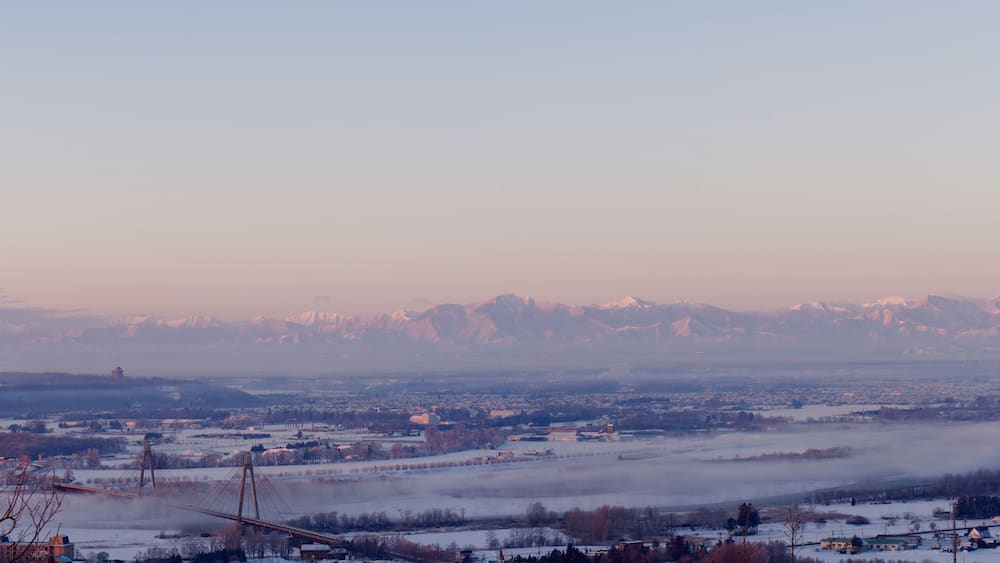 Un paysage enneigé avec un pont, des montagnes et une ville en arrière-plan.
