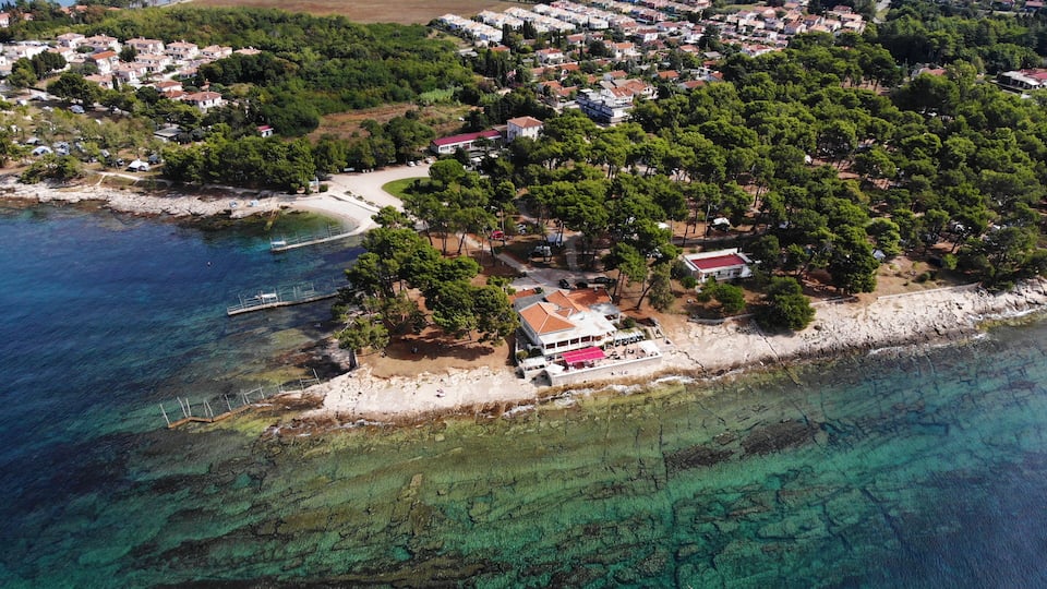 An aerial view of a coastal town with a beach, clear waters, and dense greenery.