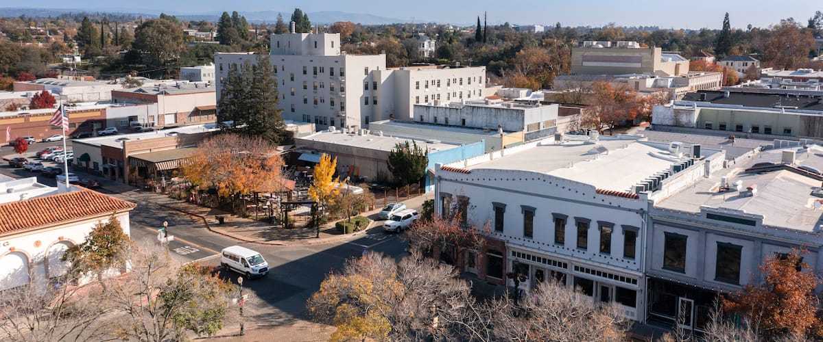 A cityscape with a mix of modern and historic buildings, a clear blue sky, and autumn-colored trees.