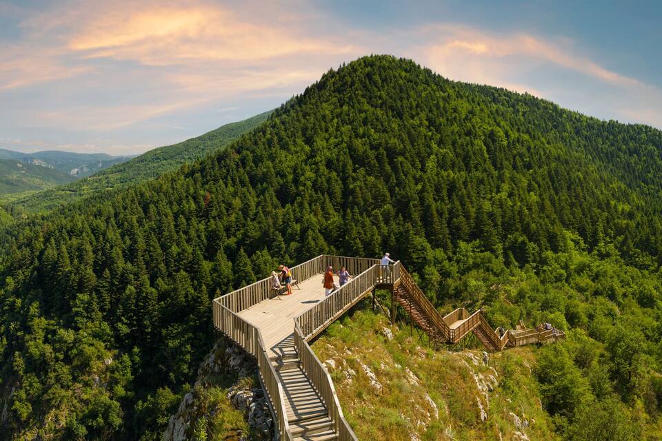 A wooden observation deck on a mountain ridge overlooking a valley with dense forests.