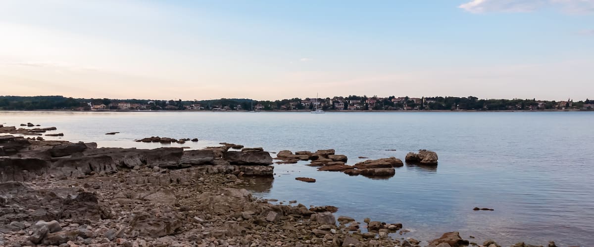 A rocky shoreline with calm water and a distant town.