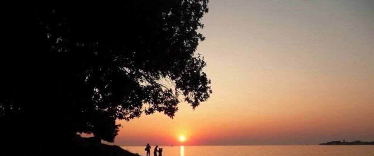 A sunset over a calm sea with silhouettes of people on a rocky shore.