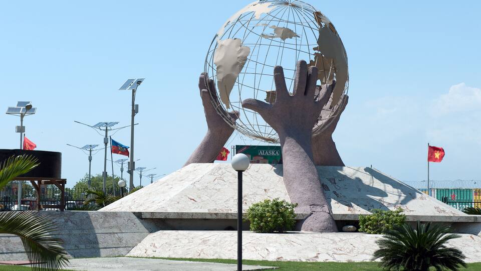 A large globe sculpture with hands holding it, surrounded by flags and solar panels.