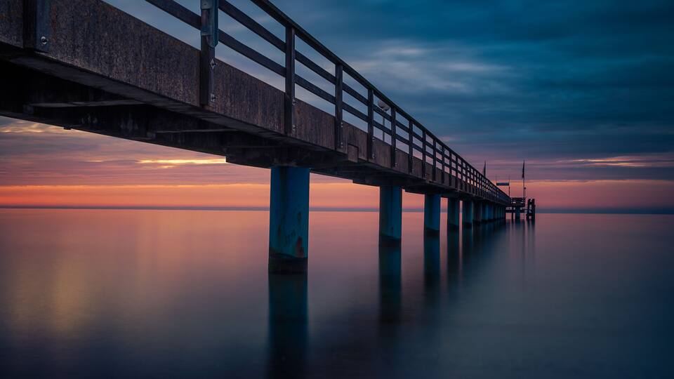 A long pier extending into calm water at sunset.