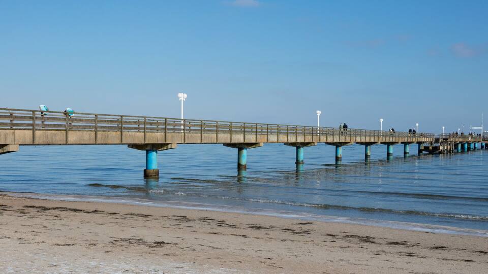 A long pier extending into the water with a sandy beach in the foreground.