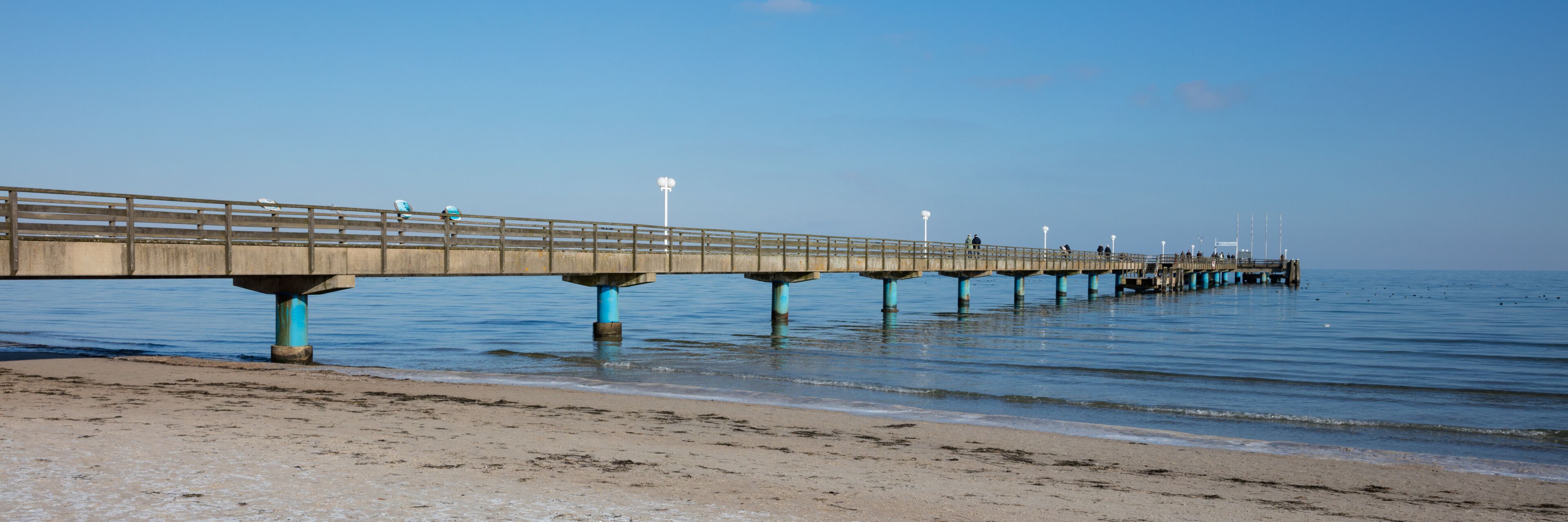 A long pier extending into the water with a sandy beach in the foreground.