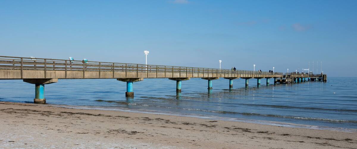 A long pier extending into the water with a sandy beach in the foreground.