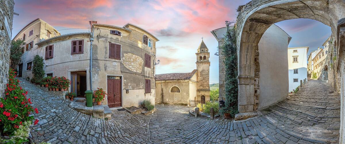 A cobblestone street with historic buildings, a church tower, and an archway.
