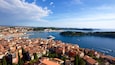 A coastal town with red-roofed buildings, a marina, and a clear blue sky.