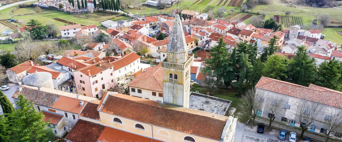A town with a prominent church tower, red-roofed buildings, and surrounding fields.