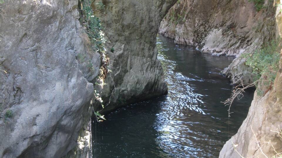 A narrow canyon with a river flowing through it, surrounded by rocky cliffs and sparse vegetation.