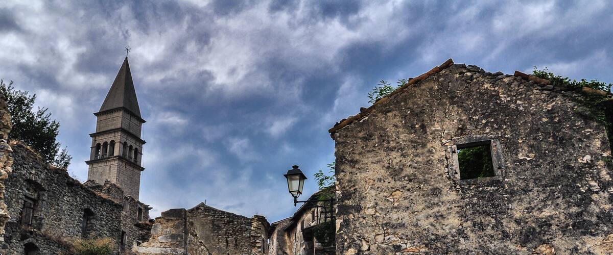 A narrow stone street flanked by old buildings, a church tower, and a street lamp.