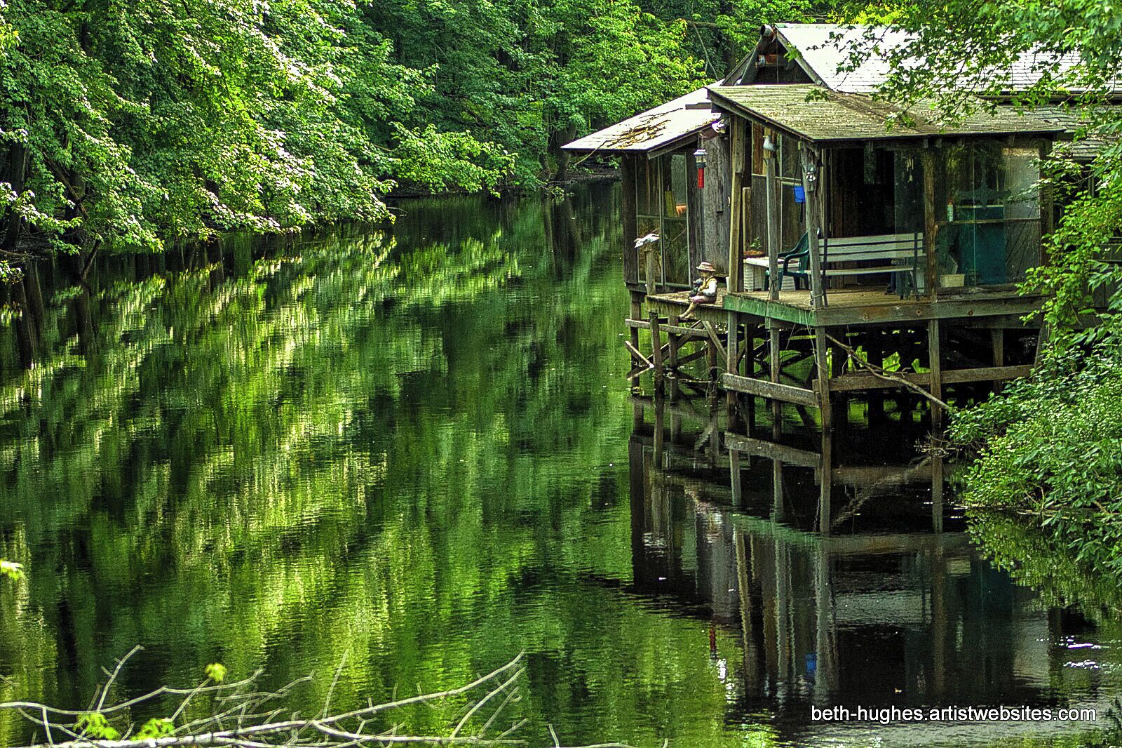 A wooden houseboat on a calm river surrounded by dense greenery.