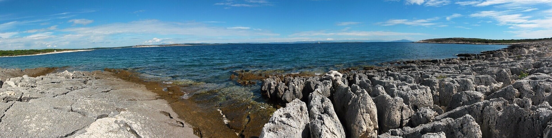 Uma costa rochosa com águas azul-claras e terra ao longe.
