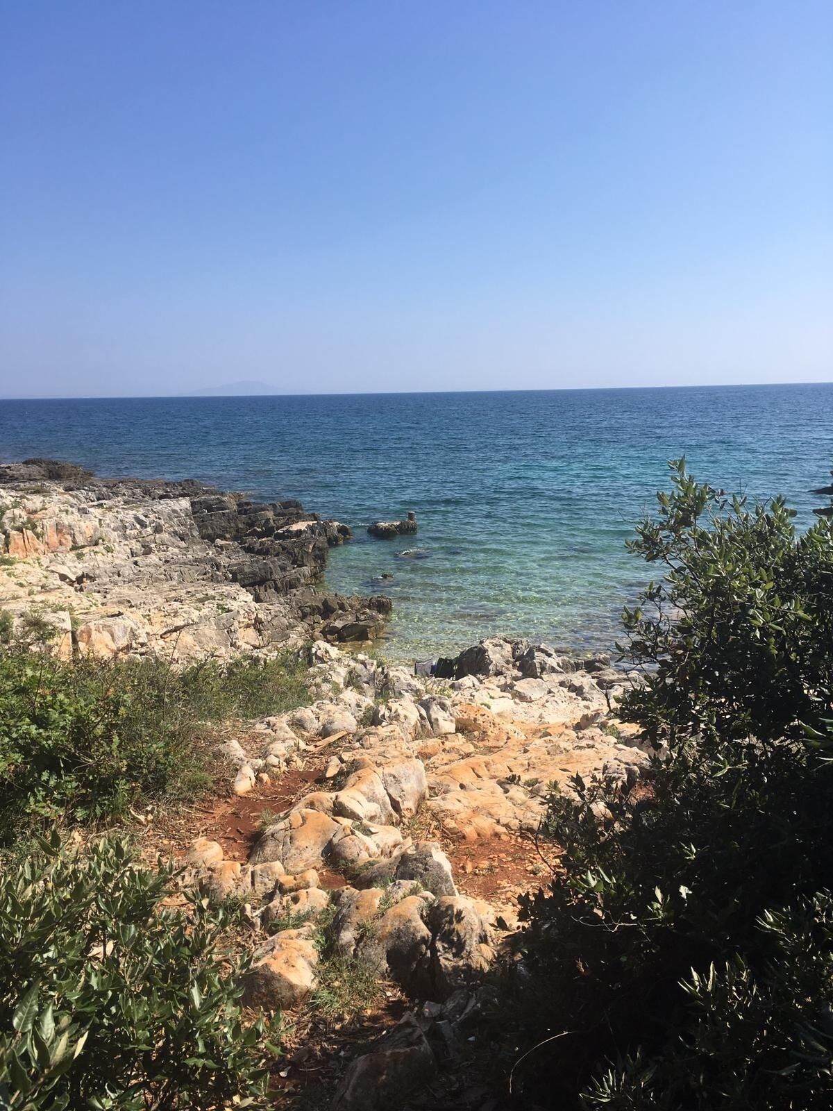A rocky coastline with clear blue sea and distant mountains.
