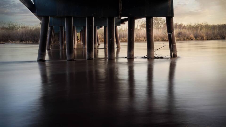 This image was a long exposure. at sunrise, of the Rio Grande River, from under a bridge.
The silhouette of the woman was added in post processing.