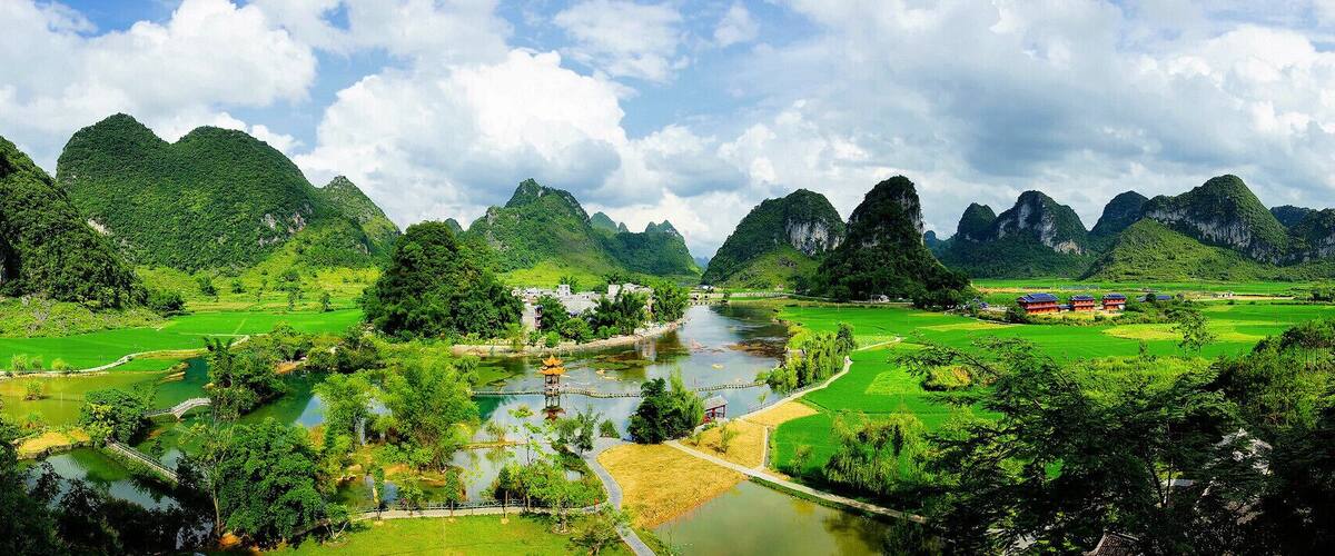 A river winding through a lush valley with green fields and traditional buildings.