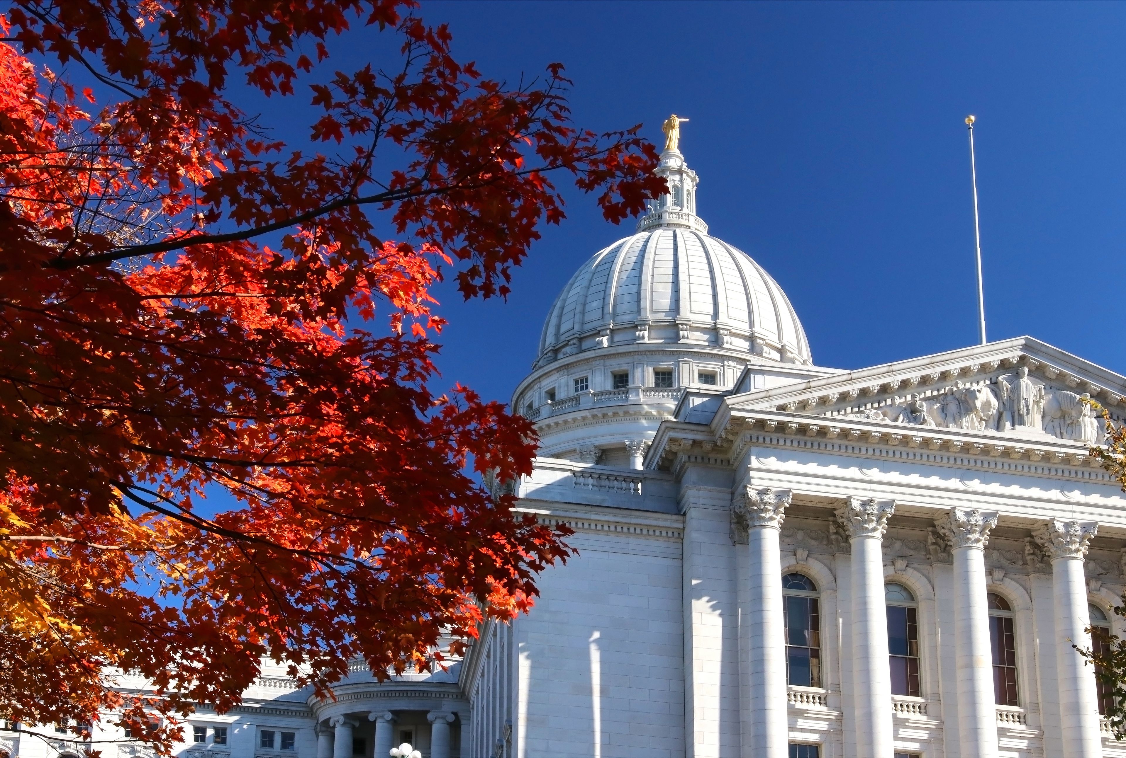A large white building with a prominent dome and columns, surrounded by autumn foliage.