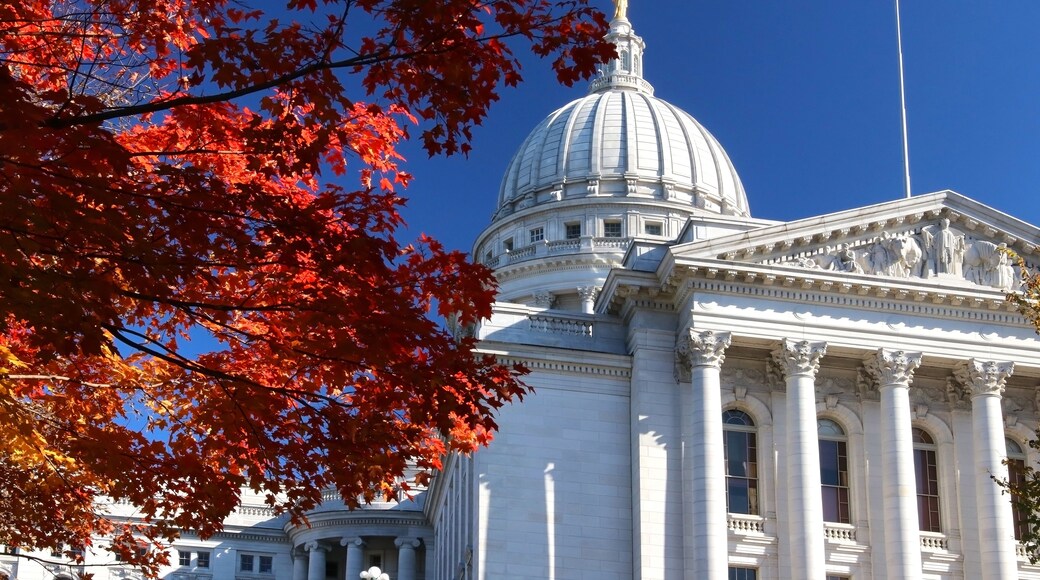 A large white building with a prominent dome and columns, surrounded by autumn foliage.
