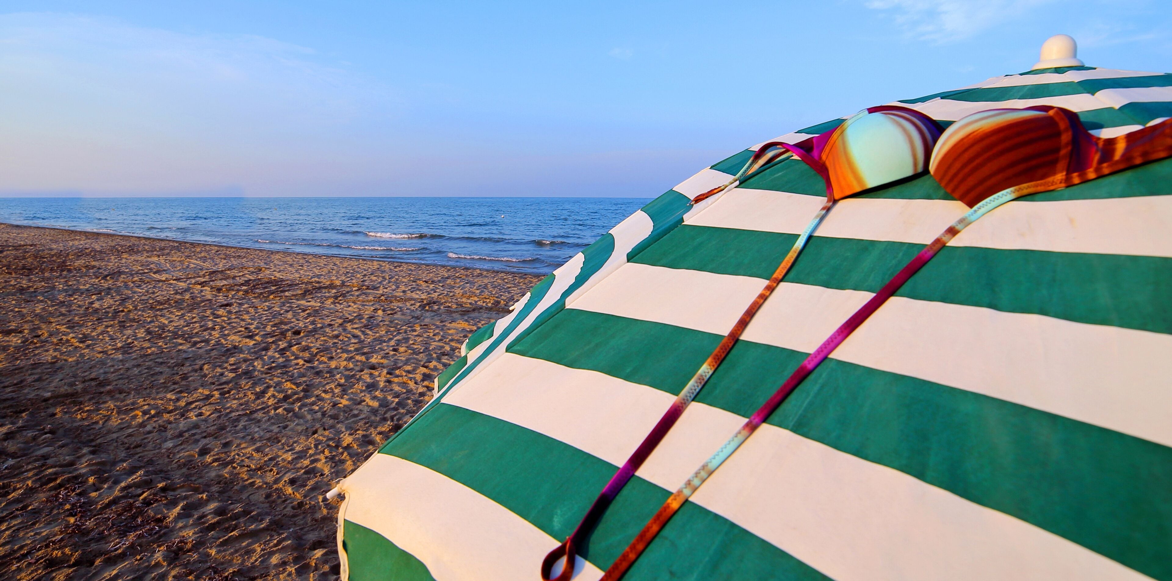 A beach with a striped beach umbrella and a colorful beach towel.