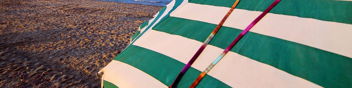 Une plage avec un parasol rayé et une serviette de plage aux couleurs vives.