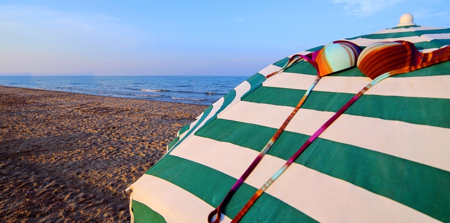 A beach with a striped beach umbrella and a colorful beach towel.