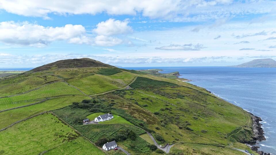 A coastal landscape with rolling hills, a white house, and a stone wall.