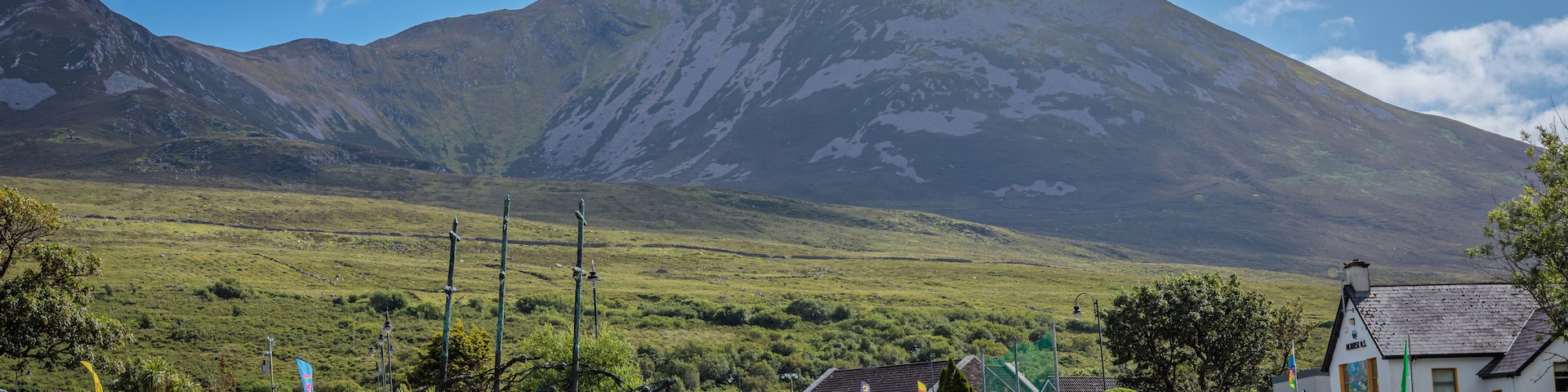 Un paisaje montañoso con un pico destacado, un campo cubierto de hierba y un edificio con un cartel.