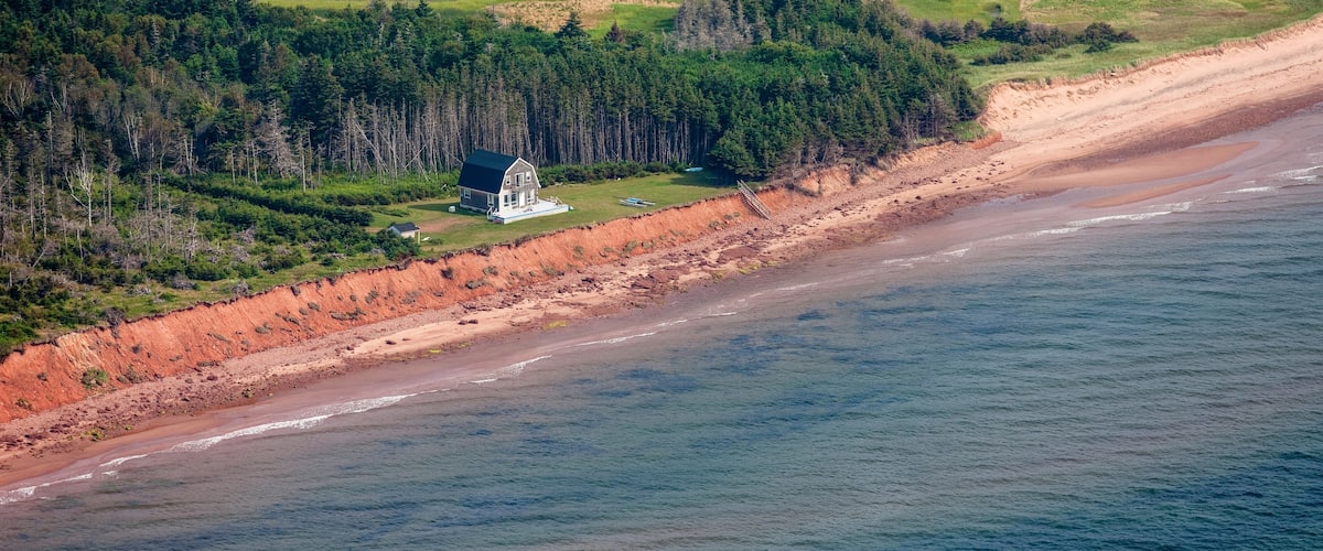A coastal landscape with a beach, forested area, and a small white house near the shore.