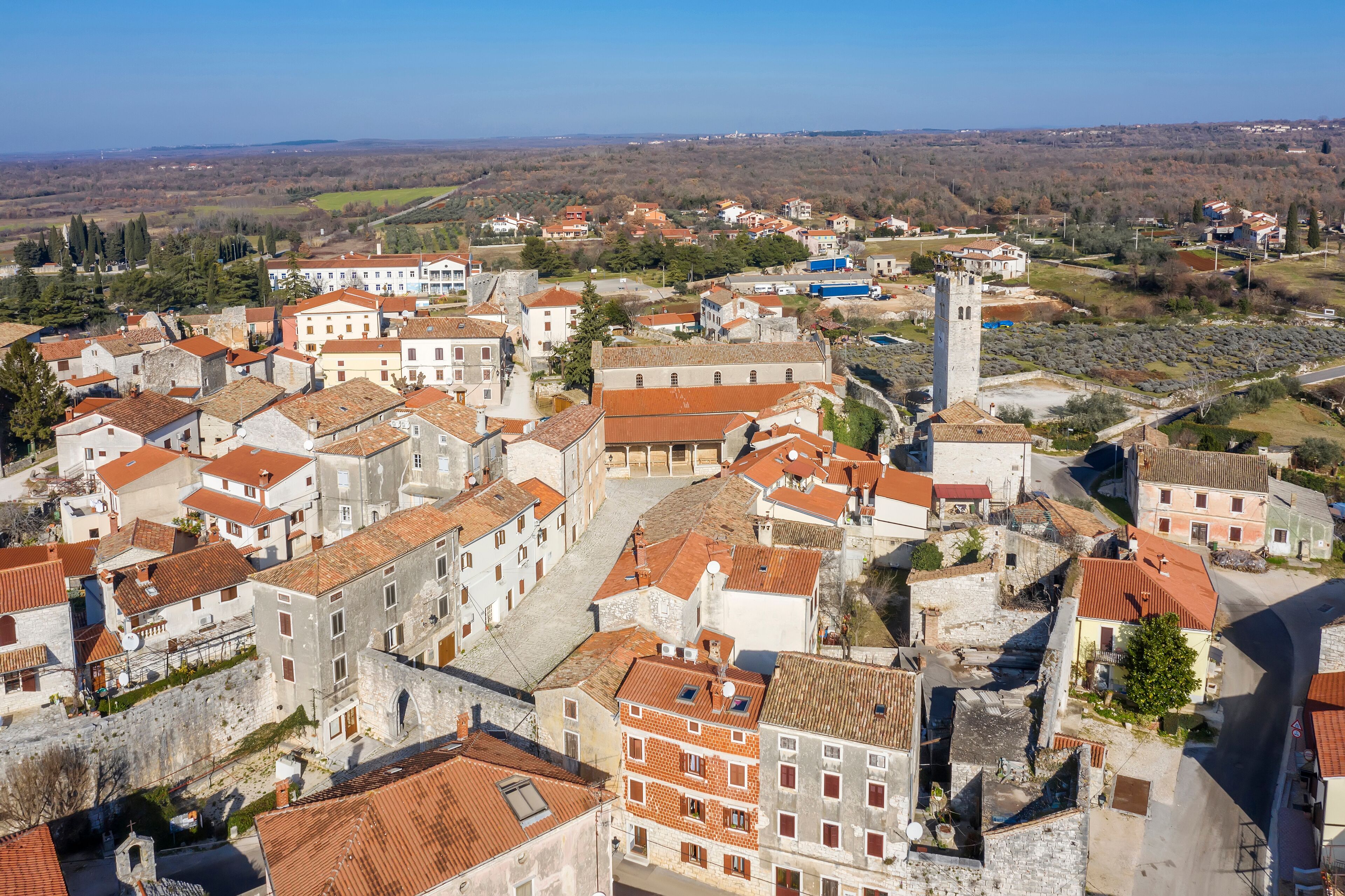 A historic town with red-roofed buildings, a prominent tower, and a hilly landscape in the background.
