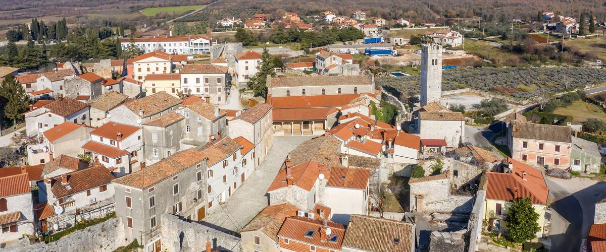 A historic town with red-roofed buildings, a prominent tower, and a hilly landscape in the background.