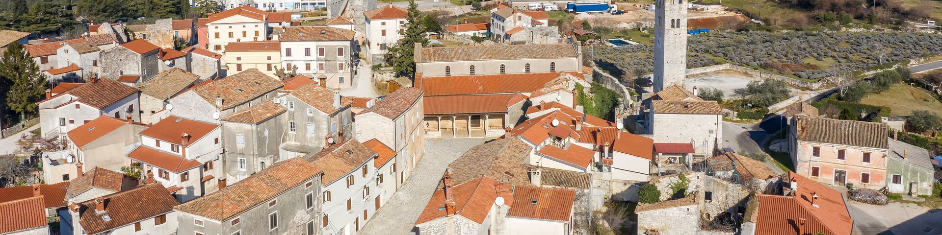 A historic town with red-roofed buildings, a prominent tower, and a hilly landscape in the background.