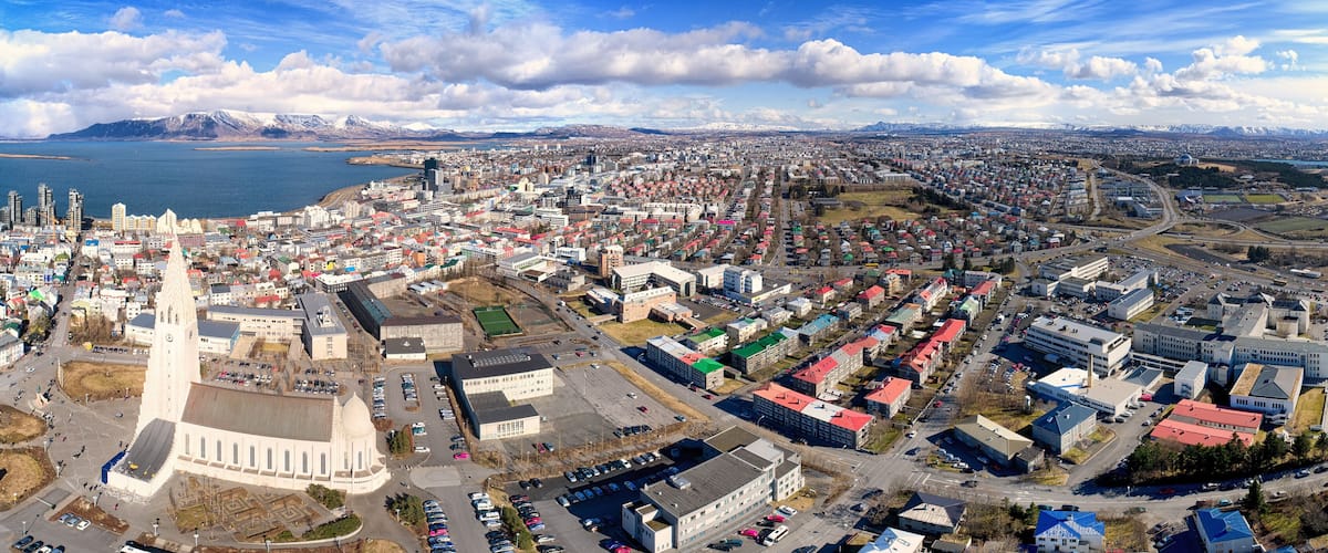 A cityscape with a prominent church, a large body of water, and snow-capped mountains in the background.