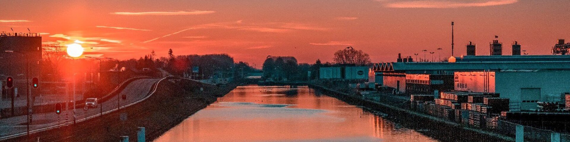 A sunset over a river with buildings on the right and a bridge in the distance.