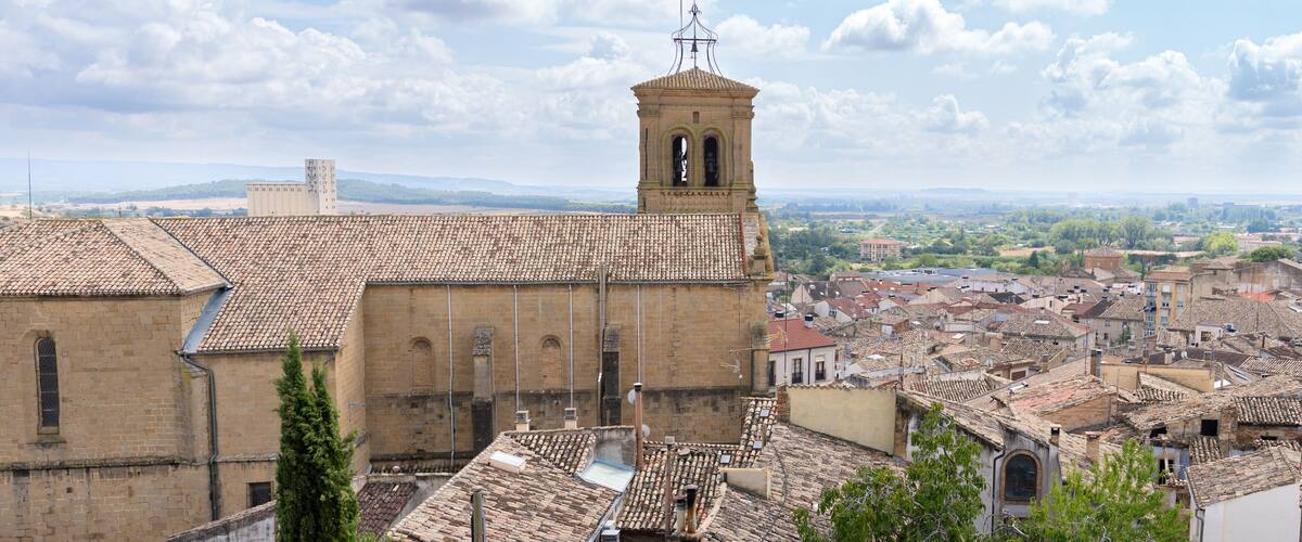 A historic church with a bell tower, surrounded by a densely built town with terracotta roofs.