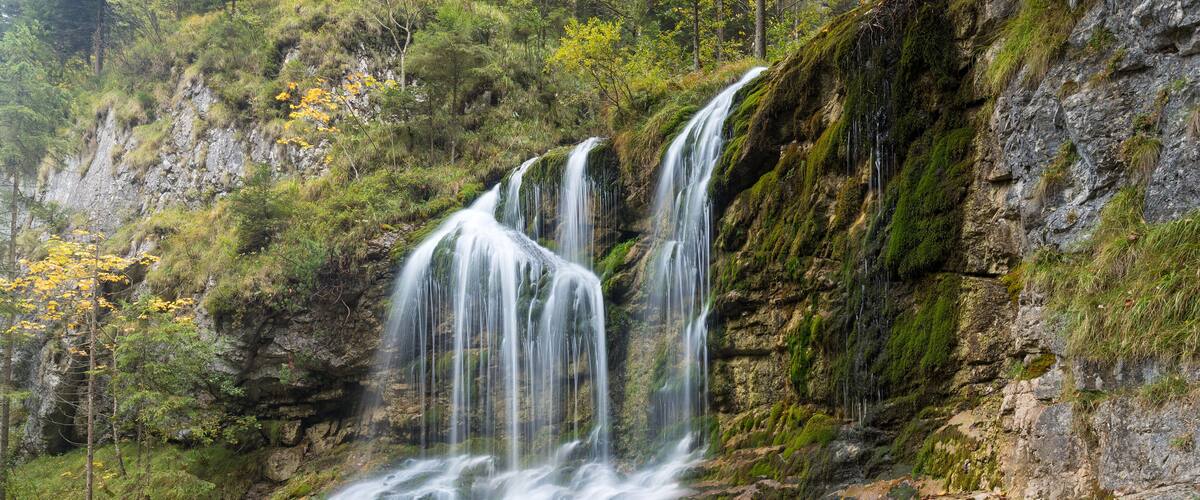 A multi-tiered waterfall cascading down a rocky cliff surrounded by lush greenery.