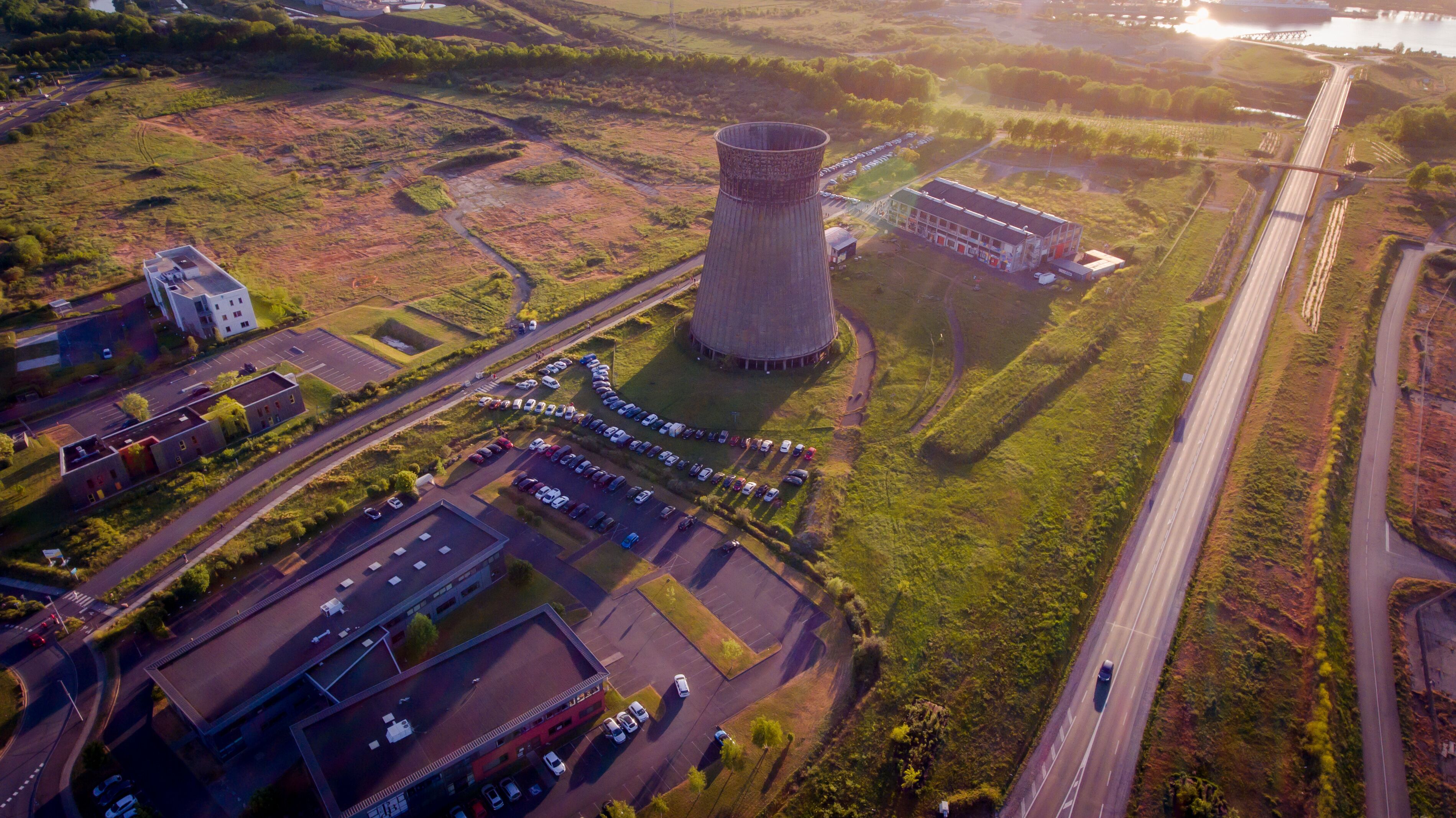 An industrial area with a large cooling tower, a parking lot, and a highway.