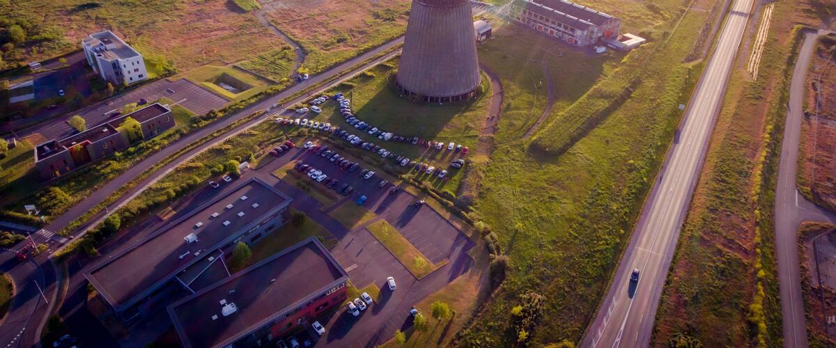 An industrial area with a large cooling tower, a parking lot, and a highway.
